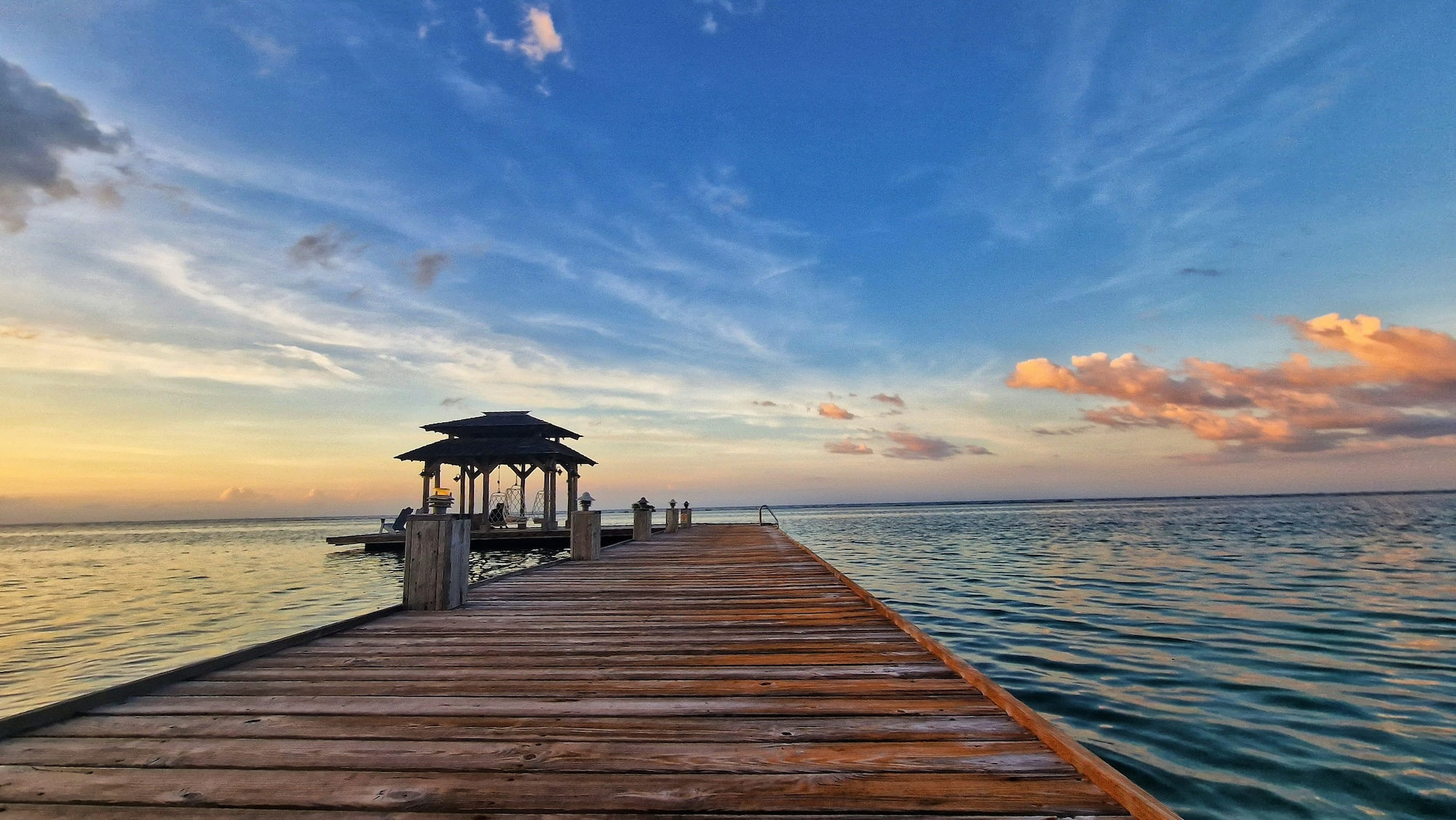 A wooden dock with a gazebo on the end of it overlooking turquoise water