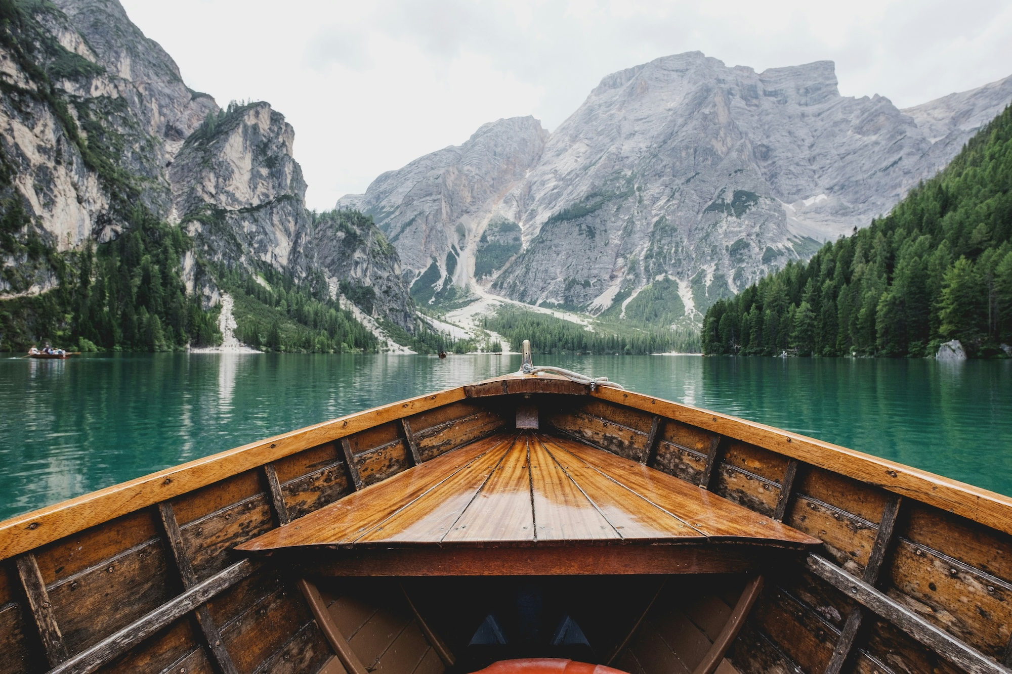 Brown wooden boat moving towards mountains on a pristine lake