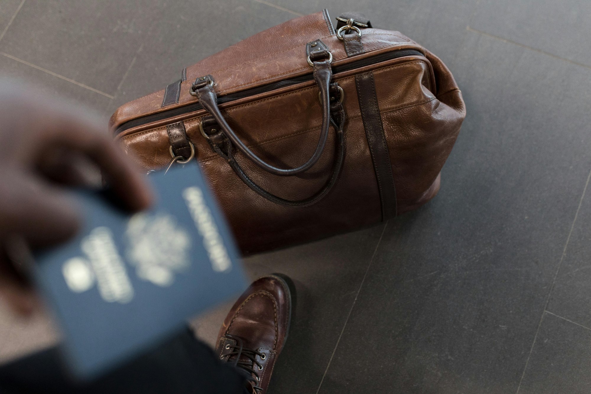 Traveler holding a passport beside a leather duffel bag
