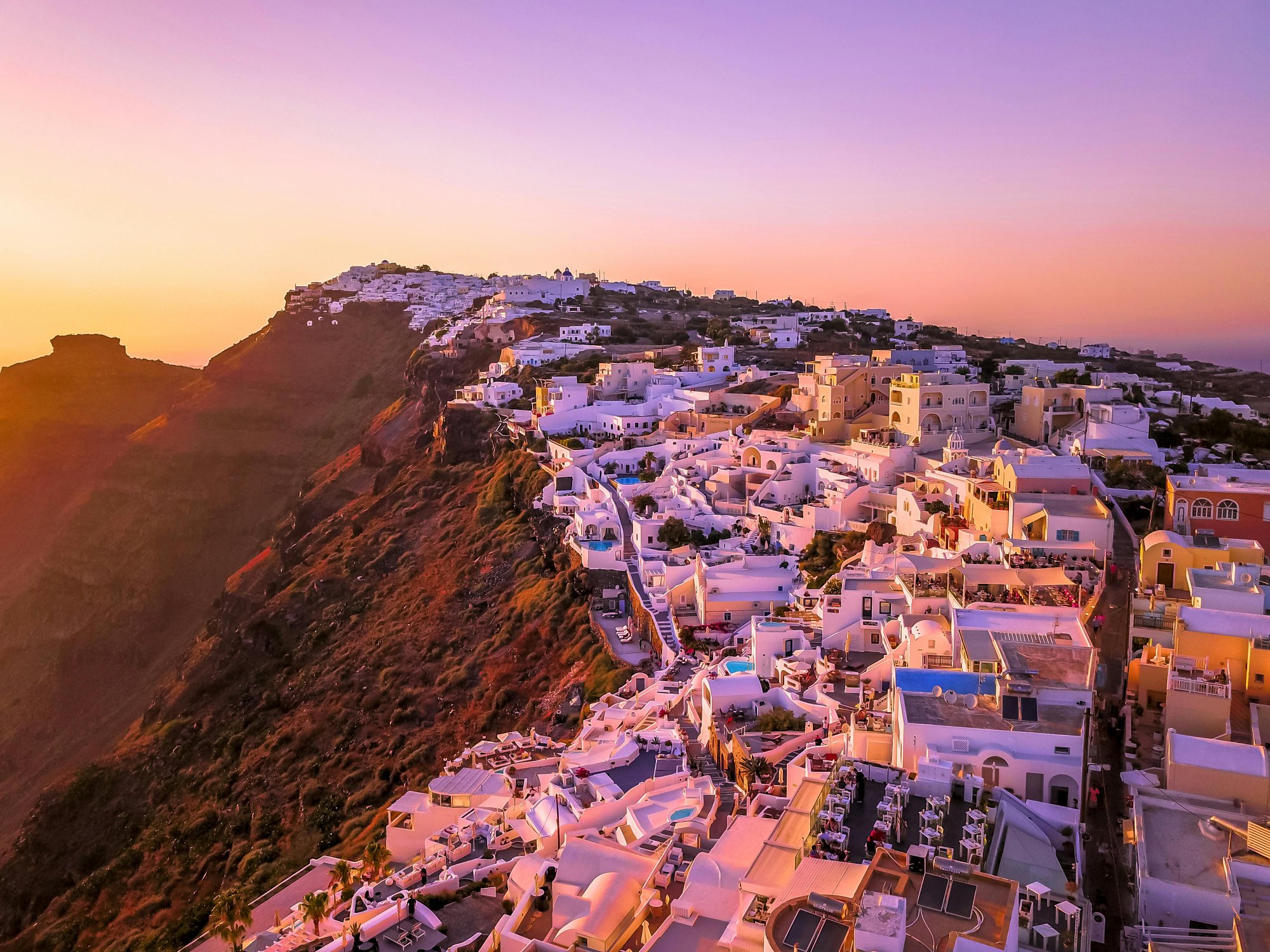 Santorini at sunset with white buildings cascading down a clifftop
