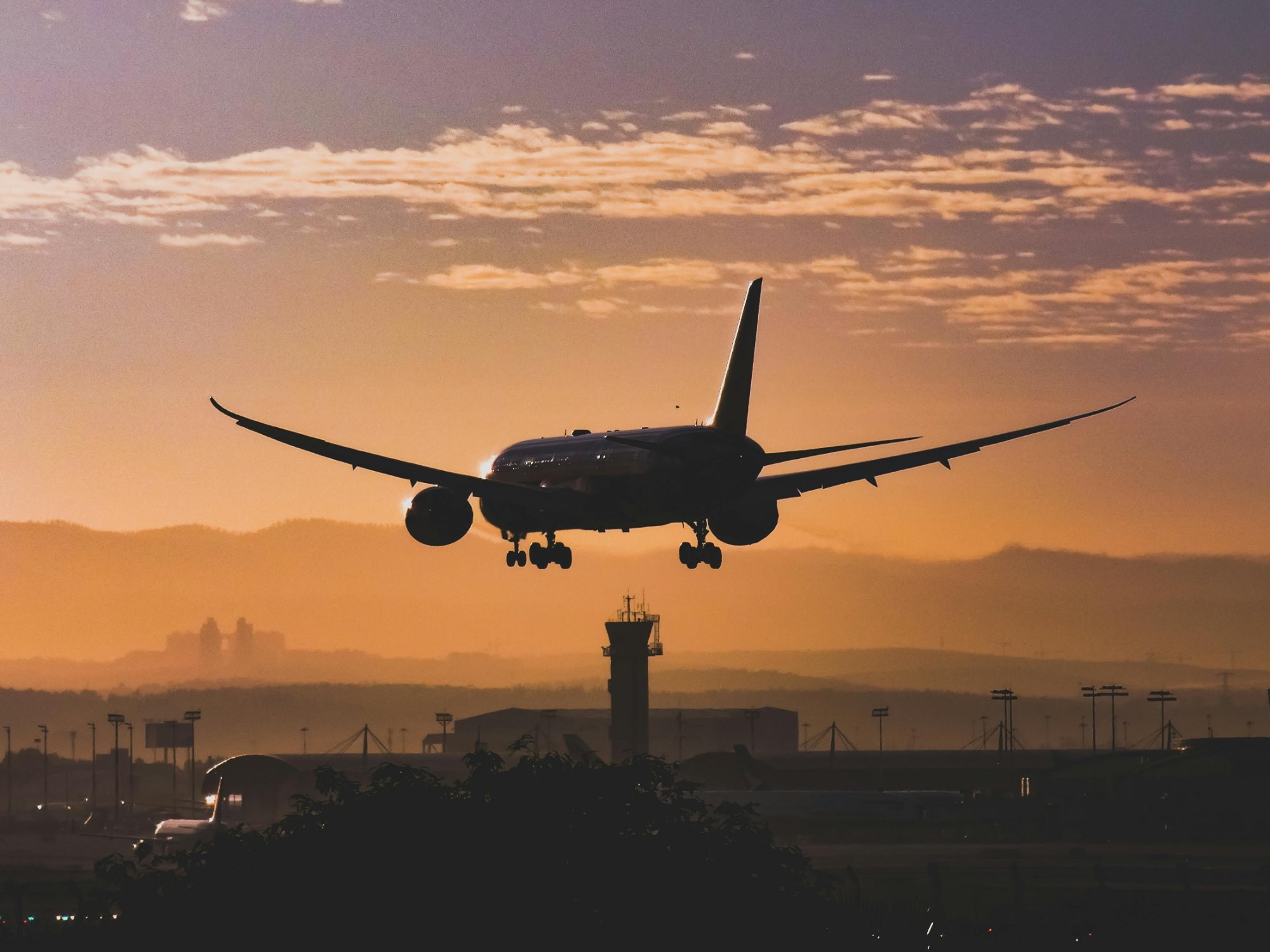 Airplane silhouette approaching runway at sunset with air traffic control tower in background