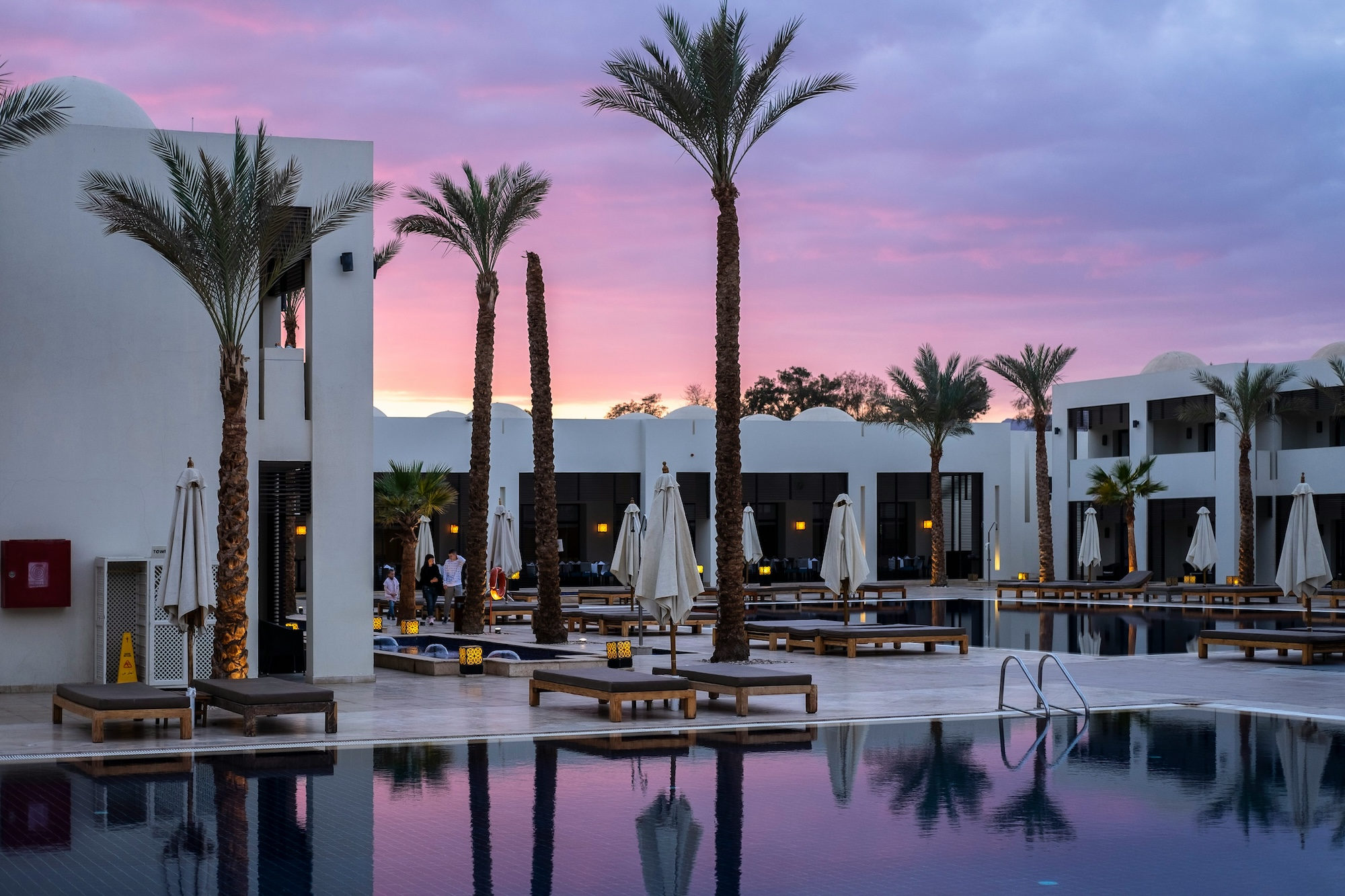 Luxury hotel pool surrounded by palm trees at sunset